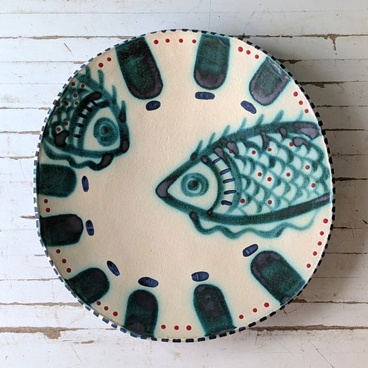 Top view of a white ceramic platter with a green fish design on a white wooden surface.