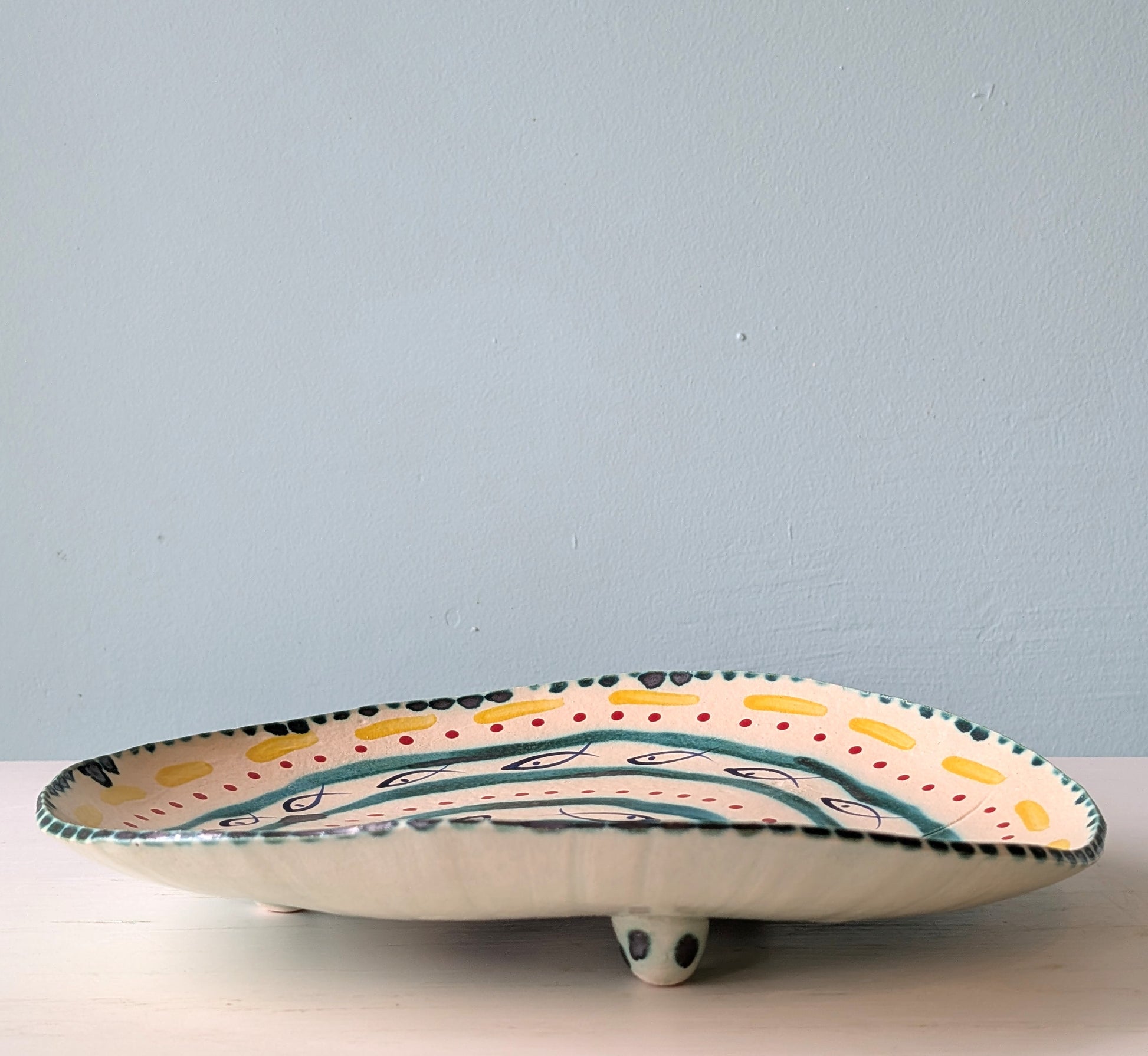Multicoloured ceramic footed platter on a white table against a blue background