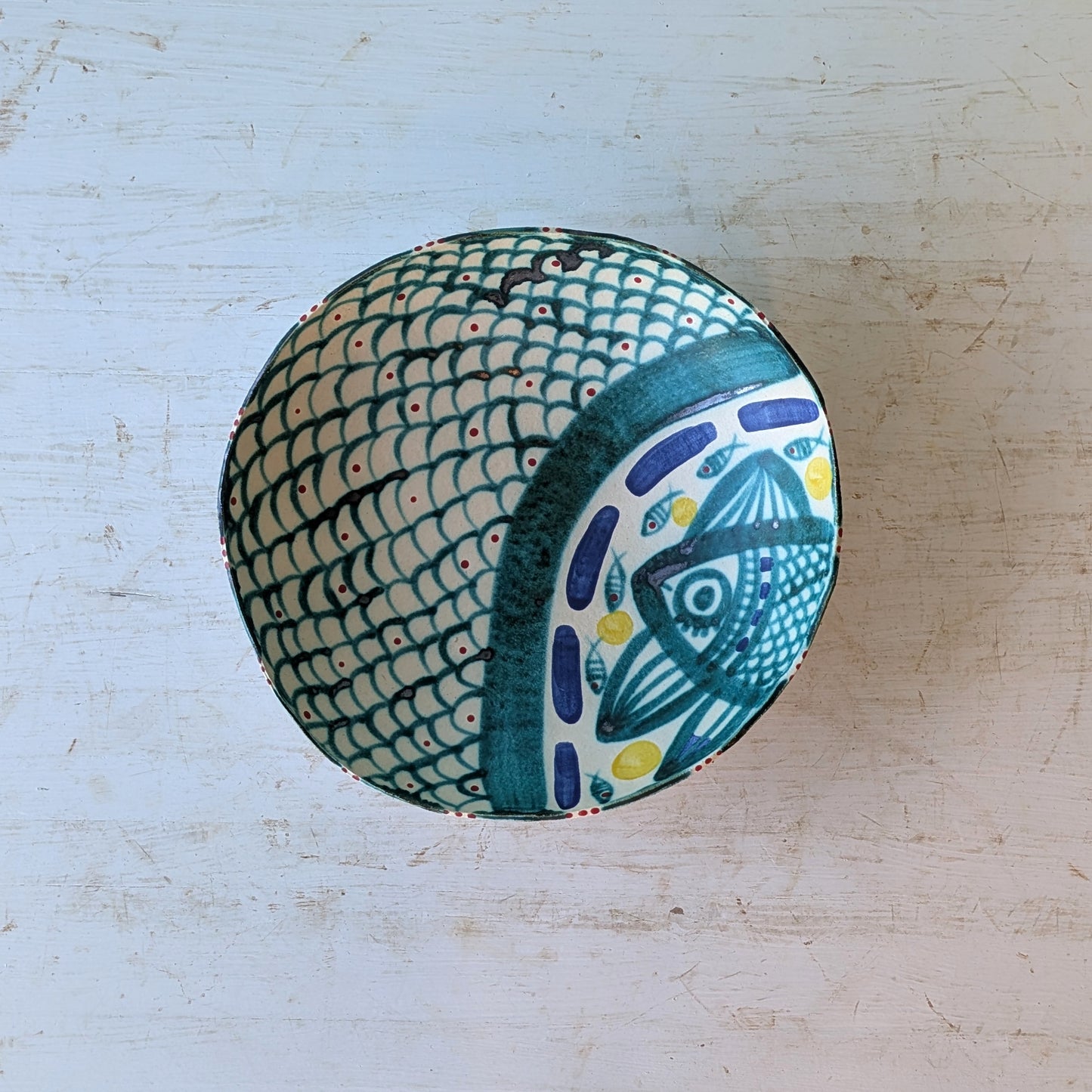 Top view of a ceramic bowl with blue, green and white fish pattern, on a white wooden table.