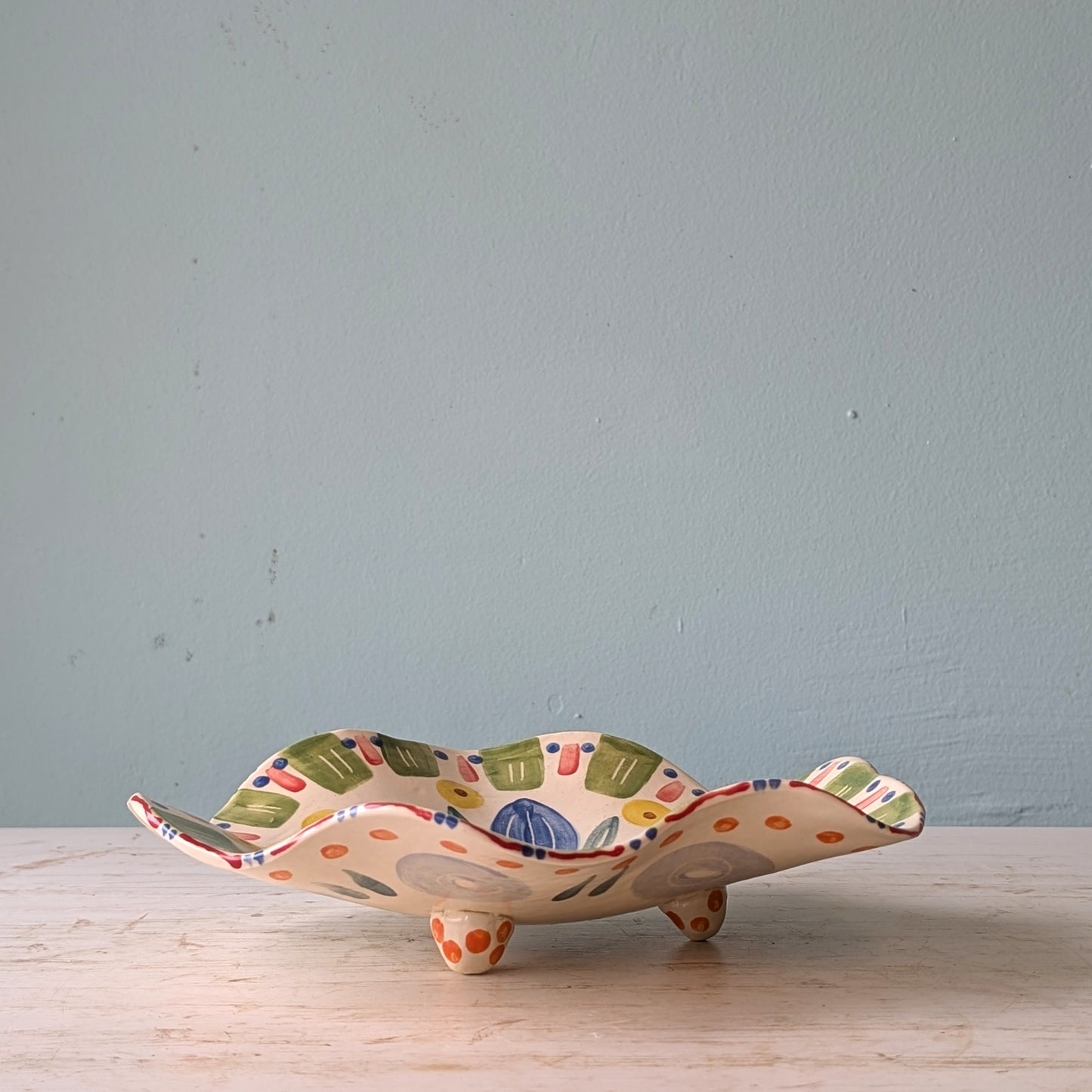Ceramic bowl with colorful design and wavy rim on a wooden surface and light blue wall background