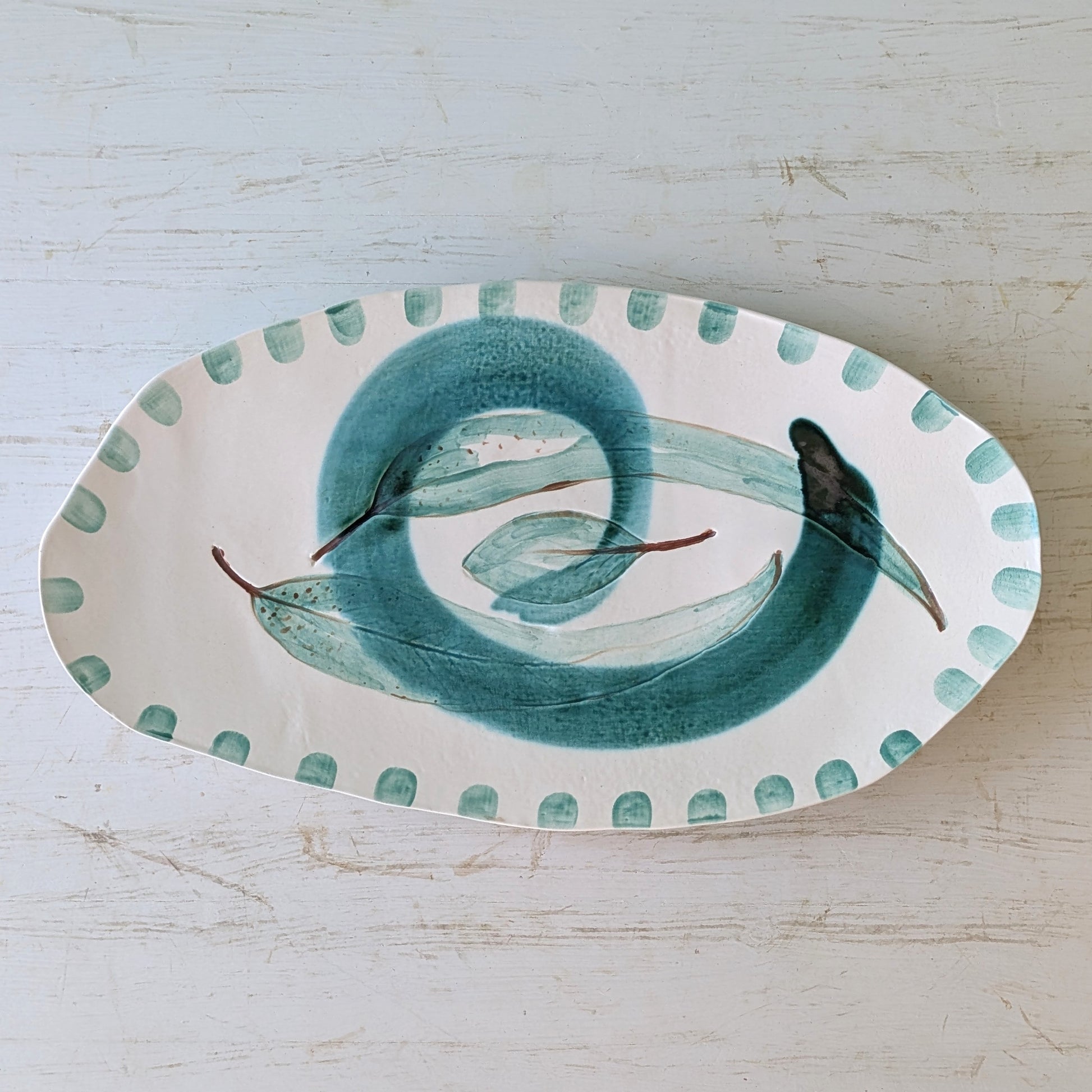 Oval ceramic platter with a green leaf design on a light wooden surface