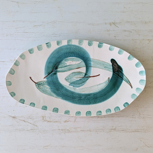 Oval ceramic platter with a green leaf design on a light wooden surface