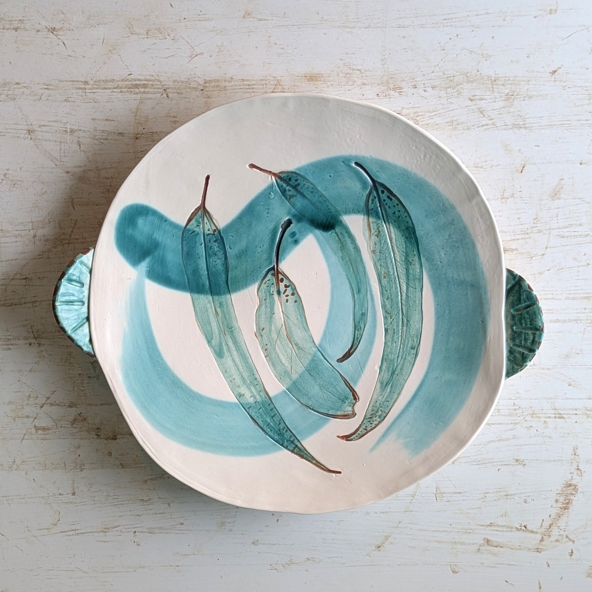 Ceramic plate with green leaf design on a light wooden surface