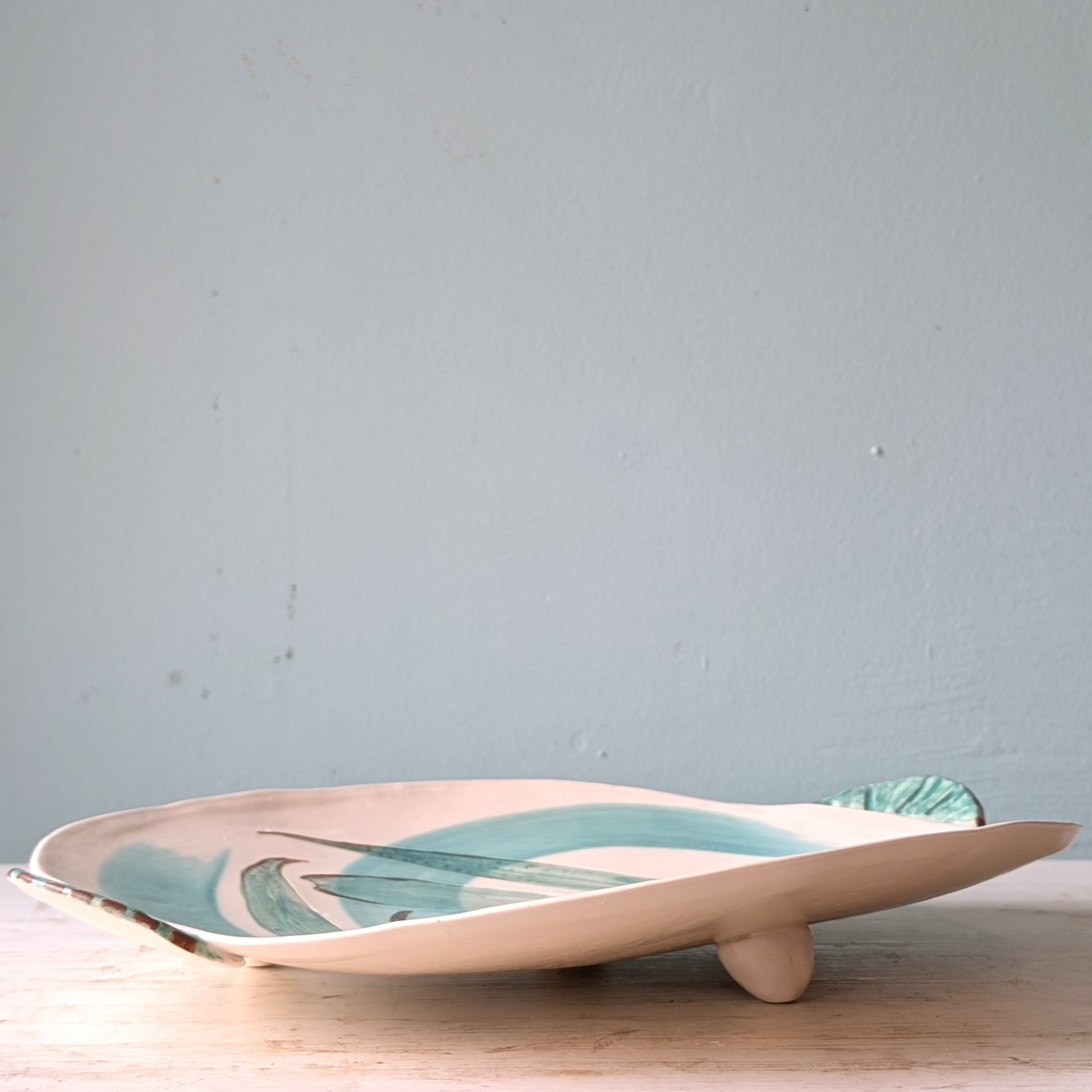 Ceramic platter with leaf design on a wooden surface against a light blue wall