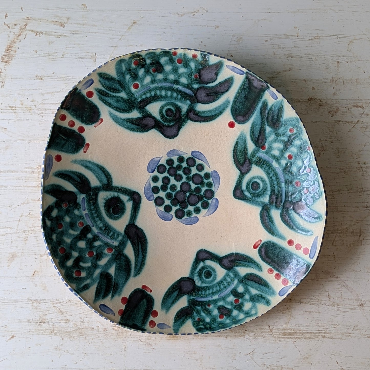 Decorative ceramic platter with fish and floral patterns on a light wooden surface