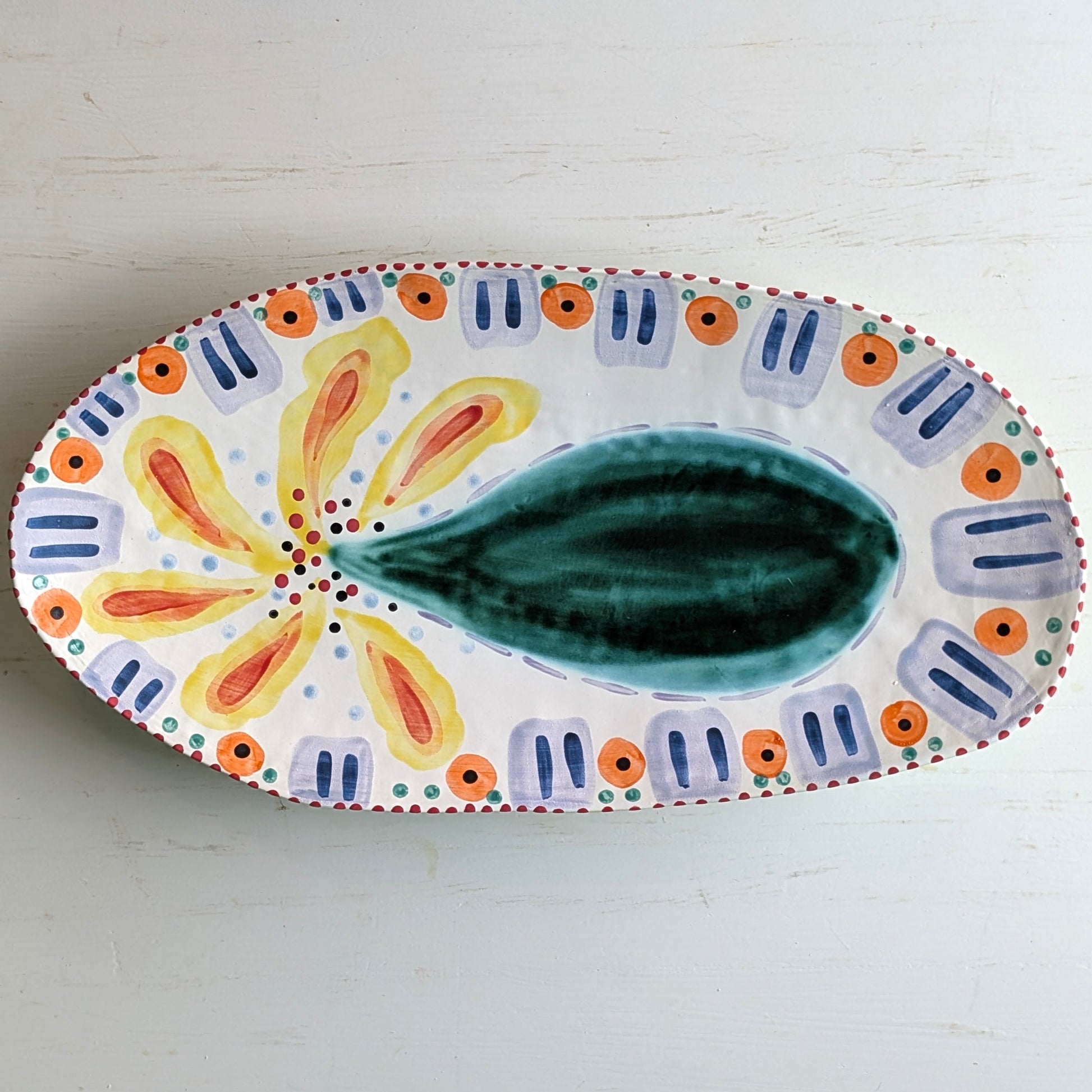 Multicoloured white ceramic platter with bottle tree pattern on a white background
