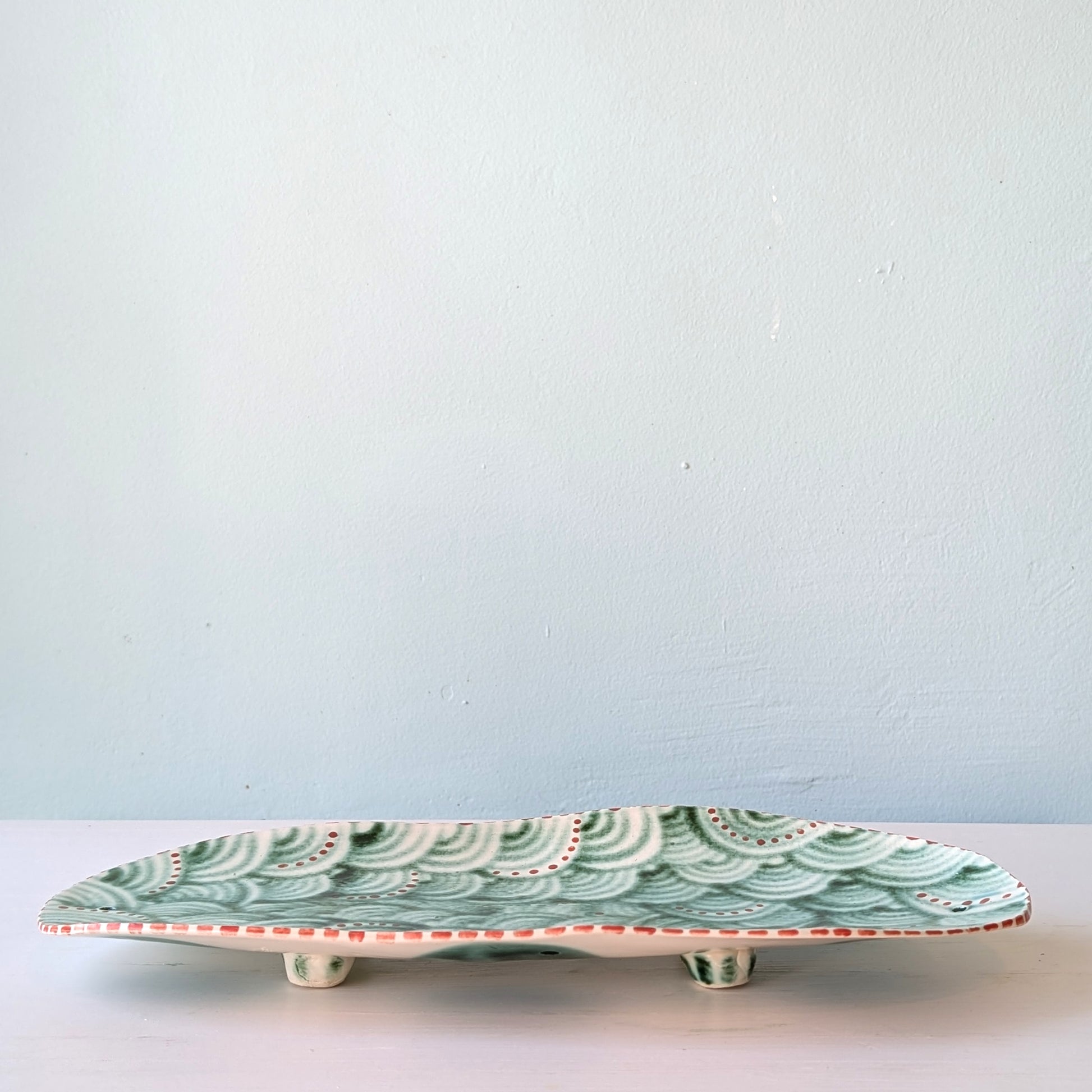 Decorative ceramic plate with green wave pattern on a light blue background
