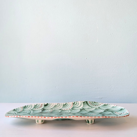 Decorative ceramic plate with green wave pattern on a light blue background