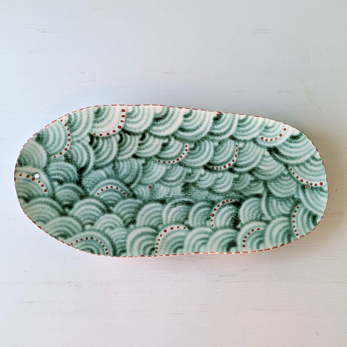Oval ceramic dish with green wave pattern on a white background