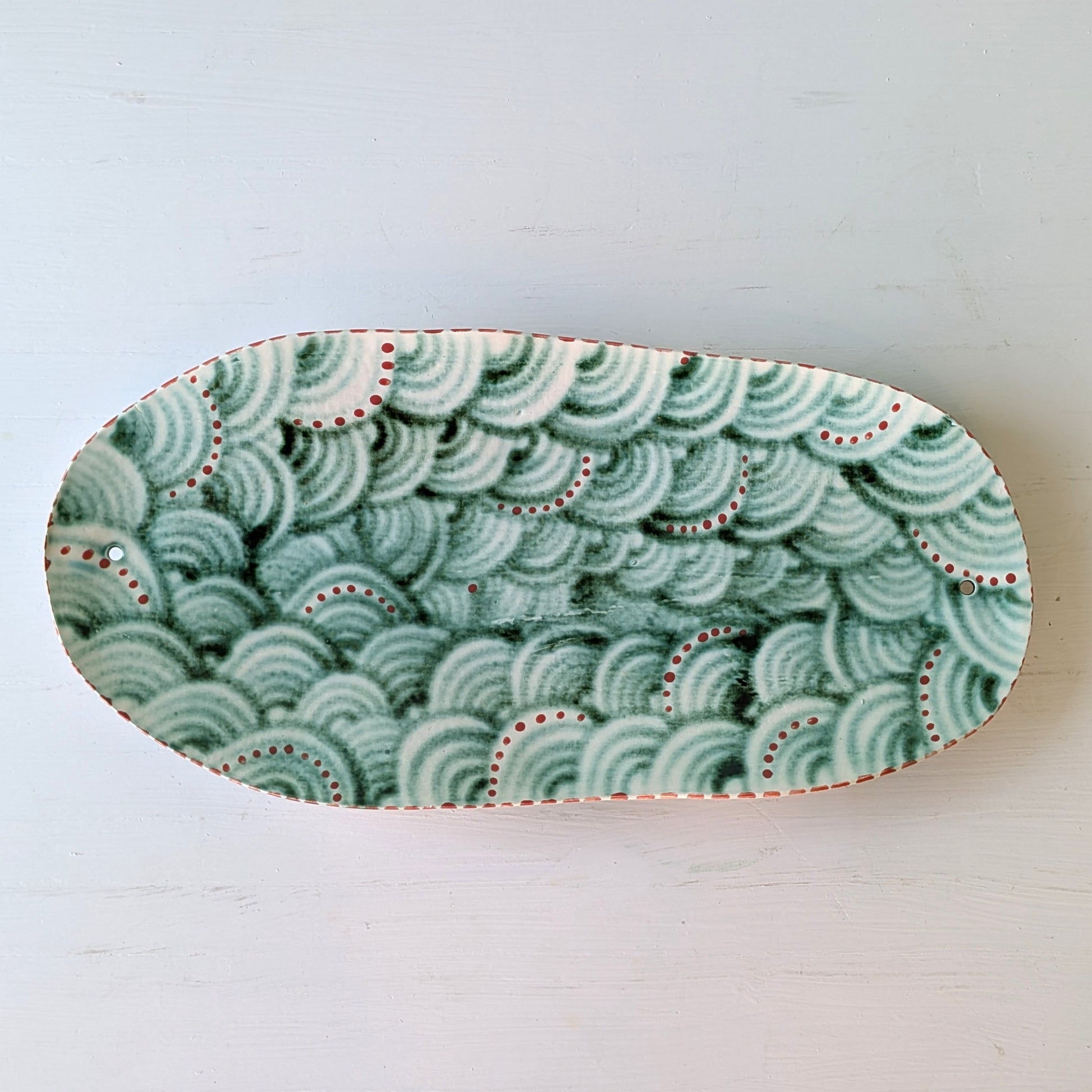 Oval ceramic dish with green wave pattern on a white background