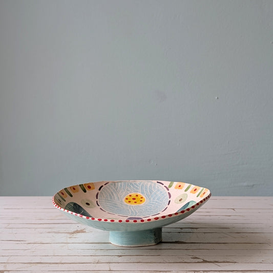 Decorative ceramic bowl with floral design on a wooden surface against a gray wall