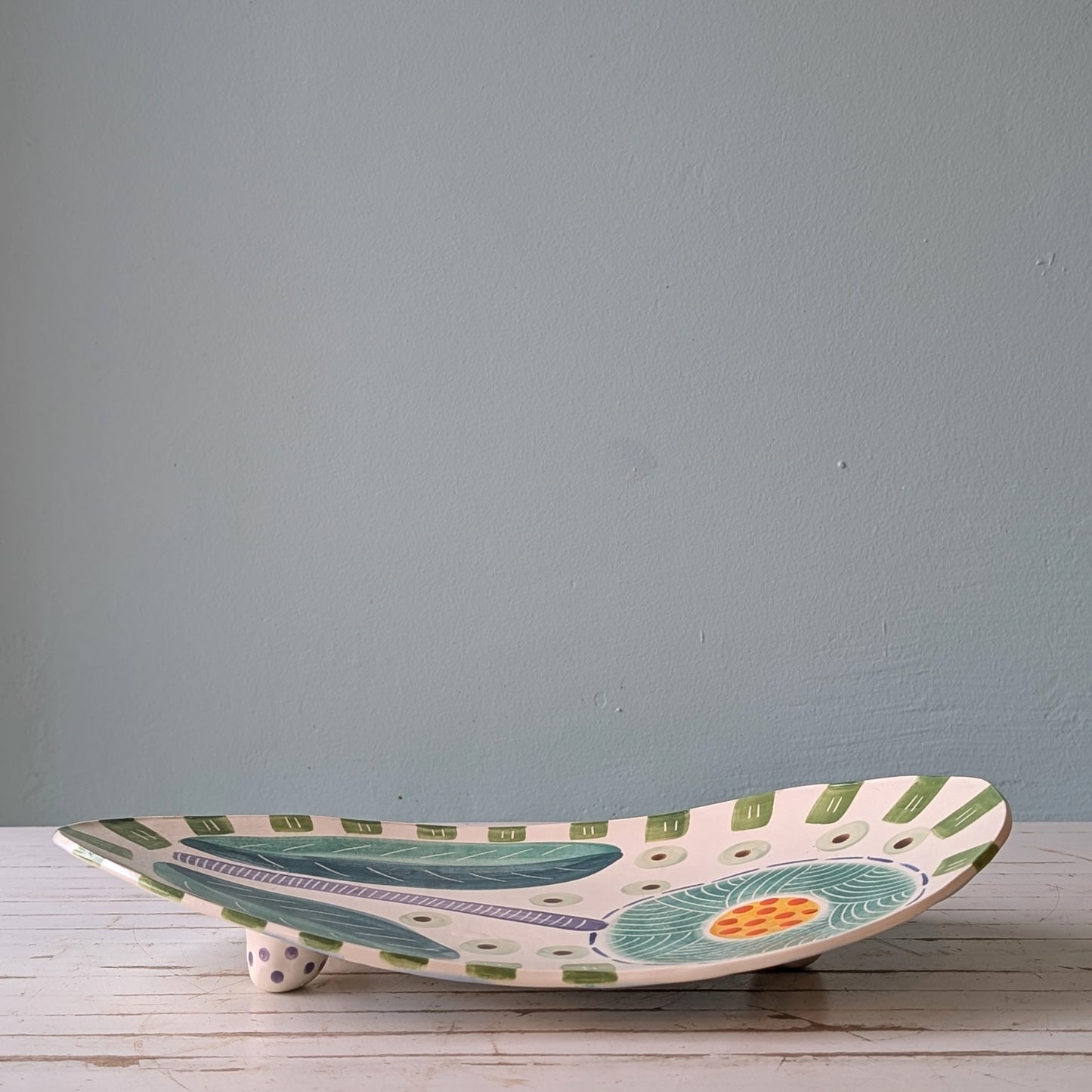 Ceramic platter with floral design on a wooden surface against a gray wall