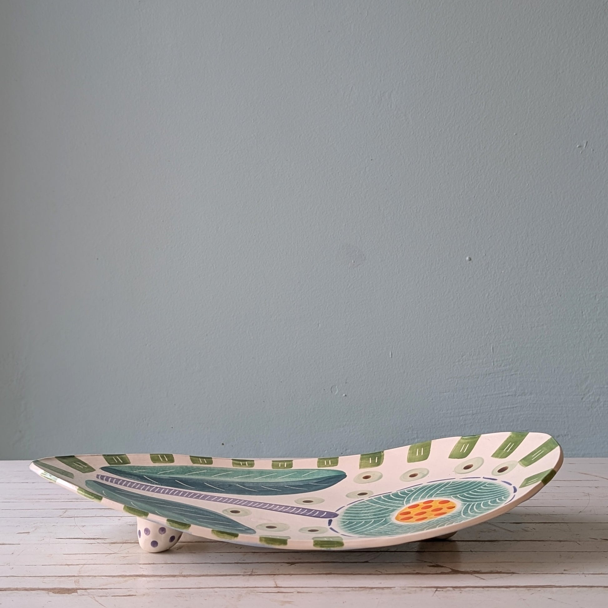 Ceramic platter with floral design on a wooden surface against a gray wall