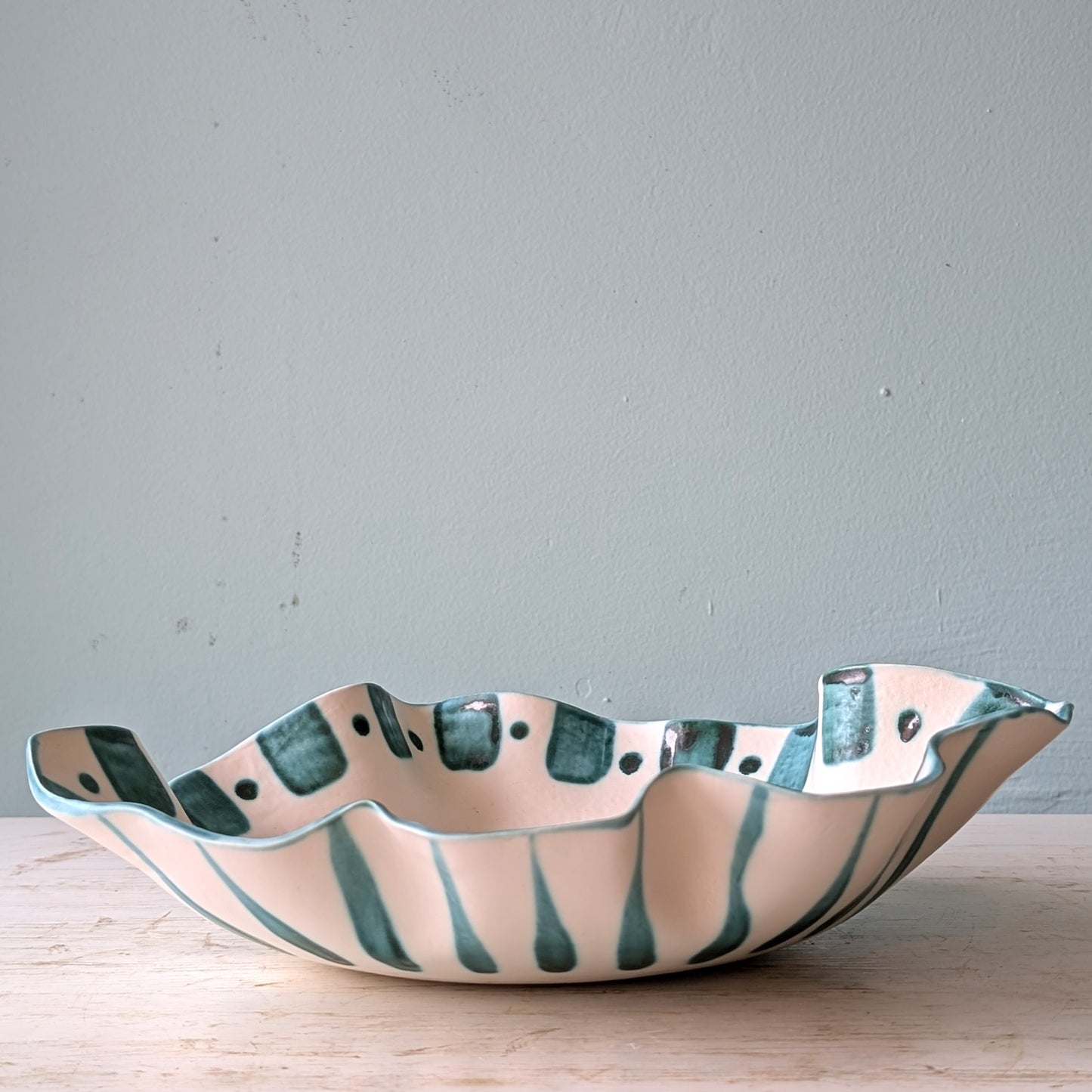 Ceramic bowl with wavy edge and green stripes on a light blue background