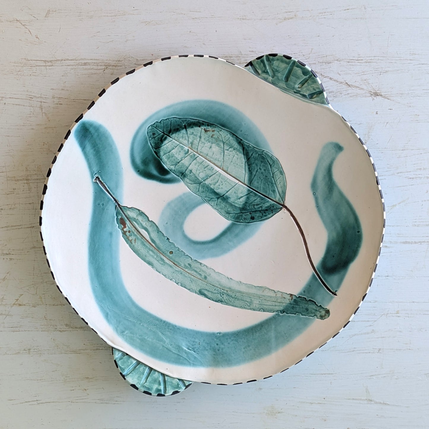 Ceramic platter with green leaf design on a light wooden surface