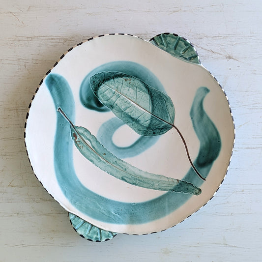 Ceramic platter with green leaf design on a light wooden surface