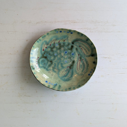 Green ceramic bowl with abstract fish design on a white table