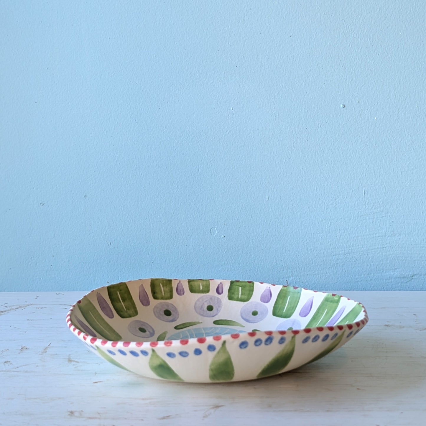 Decorative ceramic bowl with green and purple patterns on a light blue background