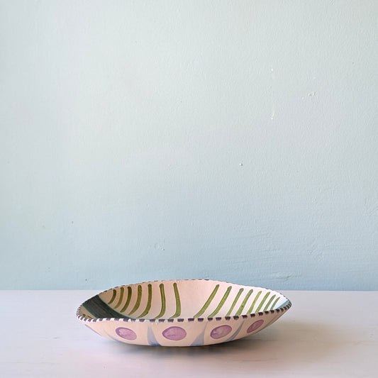 Decorative ceramic bowl with polka dot and stripe pattern on a light blue background
