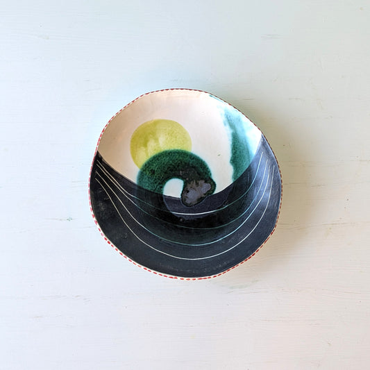 Decorative ceramic bowl with blue, green and yellow wave pattern on white table