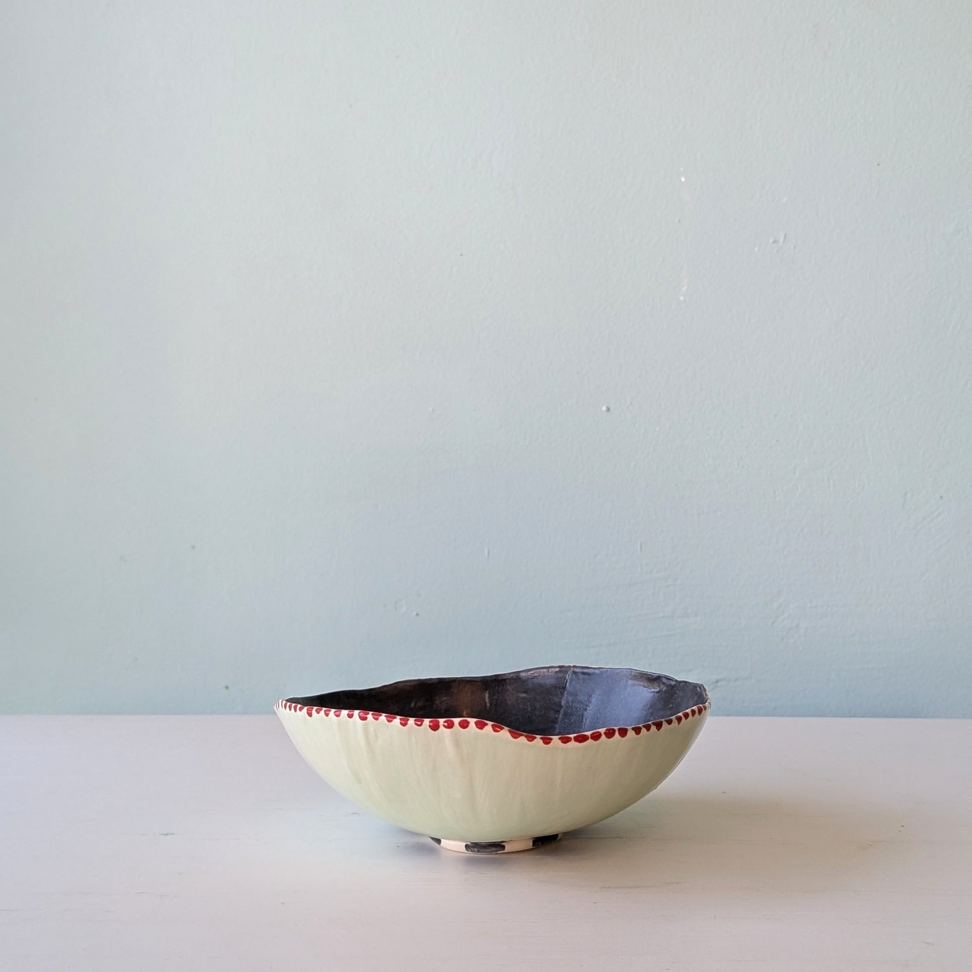 Ceramic bowl with red rim on a white surface and light blue wall background