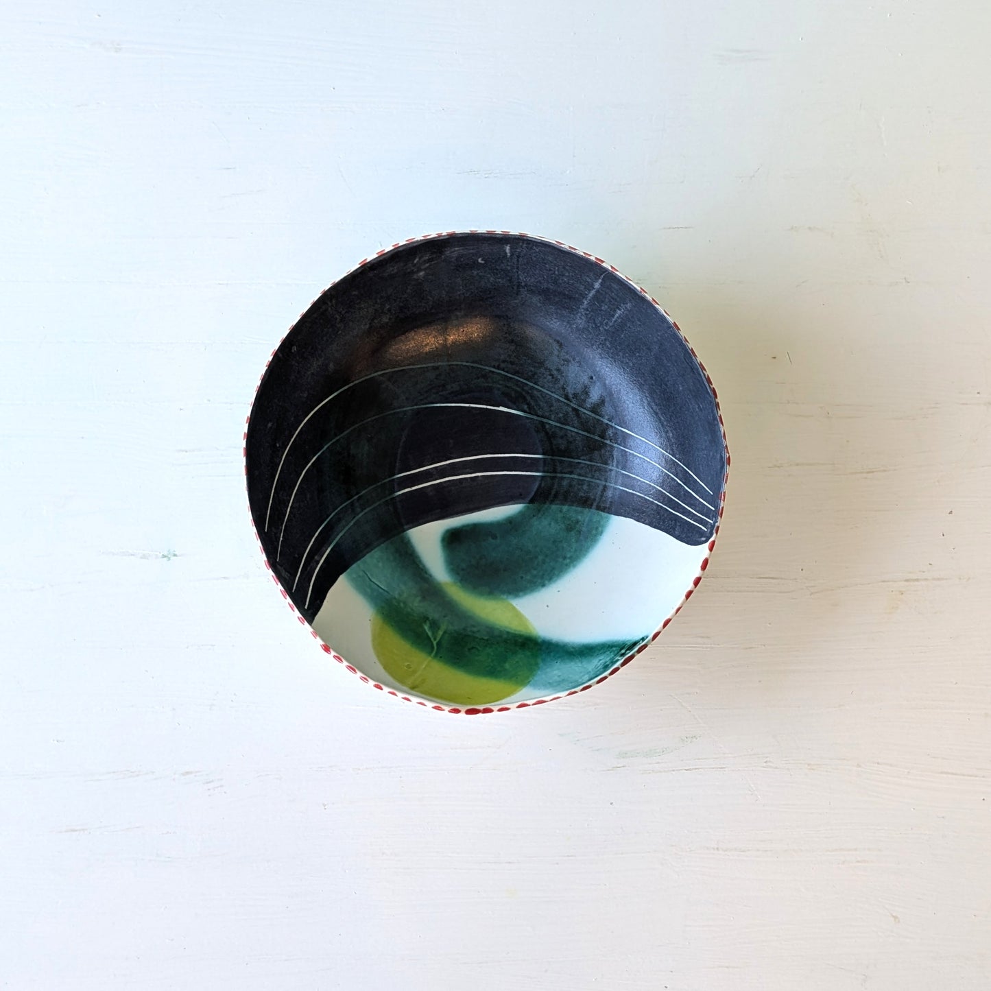 Ceramic bowl with black, green, and white design on a light wooden surface