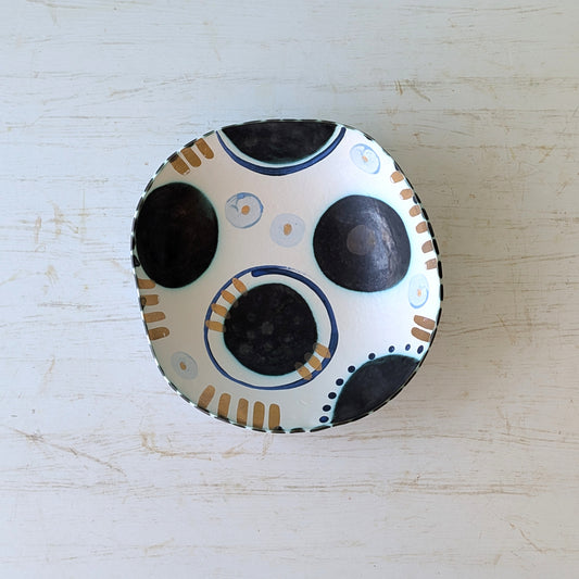 Round ceramic bowl with black and beige design on a light wooden surface