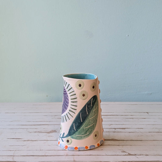 Front view of a ceramic pourer with green, blue, orange and purple botanical pattern