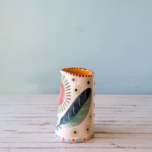Front view of a white ceramic pourer with green, blue and orange botanical pattern and orange exterior