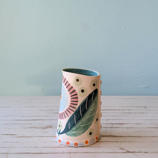 Side view of a white ceramic pourer with green, blue and orange botanical pattern and blue interior