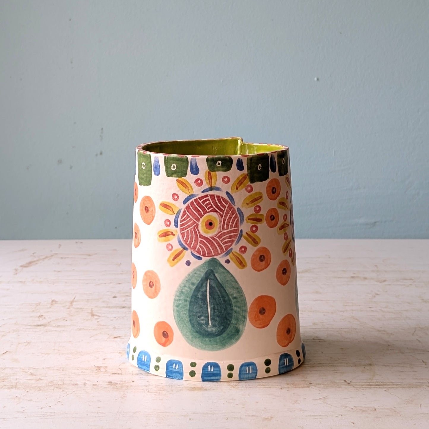 Decorative ceramic vase with colorful patterns on a wooden surface and light blue background