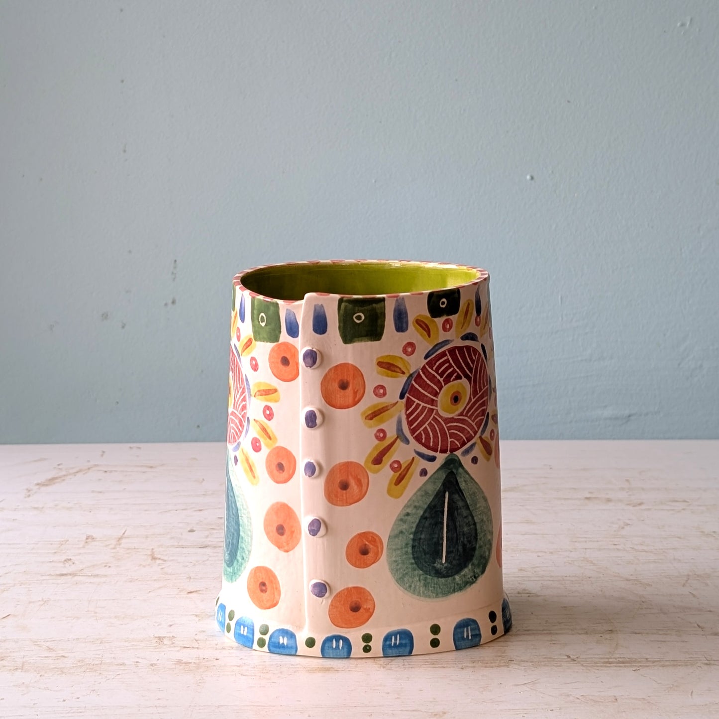 Decorative ceramic vase with colorful patterns on a wooden surface and light blue background