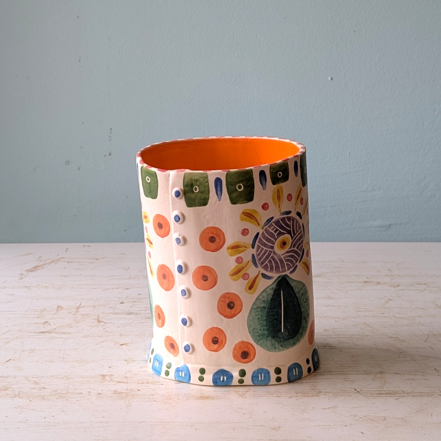 Ceramic vase with colorful patterns on a wooden surface and light blue background