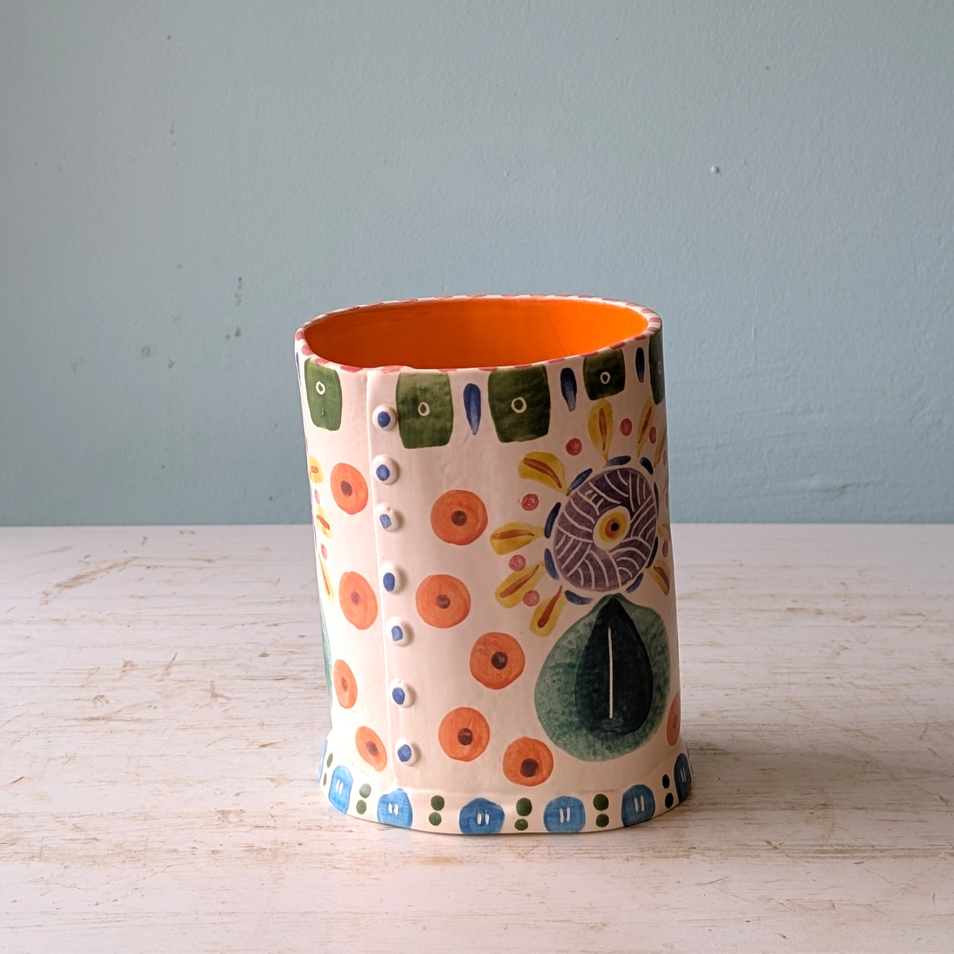 Ceramic vase with colorful patterns on a wooden surface and light blue background