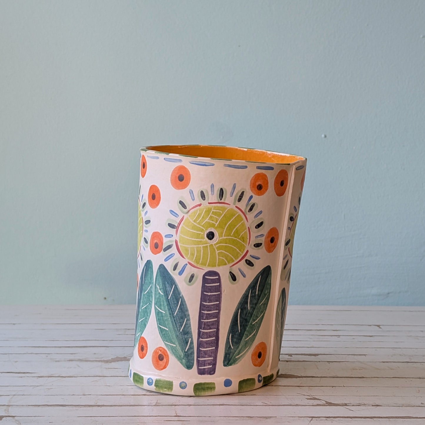 Side view of a white ceramic vase witth purple, yellow, orange, blue and green botanical pattern and orange interior