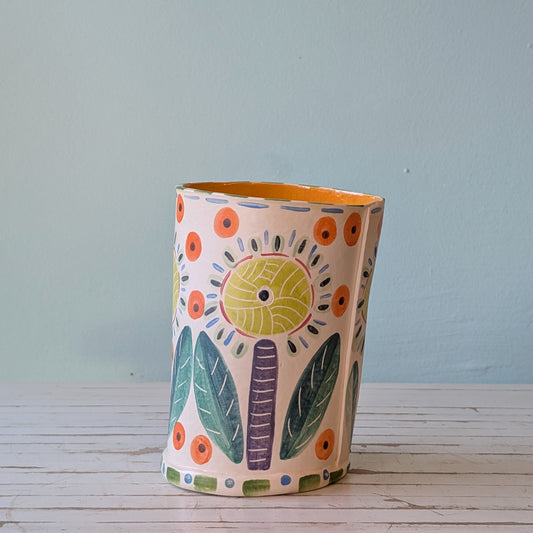 Side view of a white ceramic vase witth purple, yellow, orange, blue and green botanical pattern and orange interior