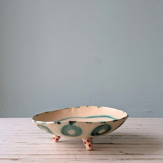 Front view of a footed ceramic bowl on a white wooden table with a blue bakcground.