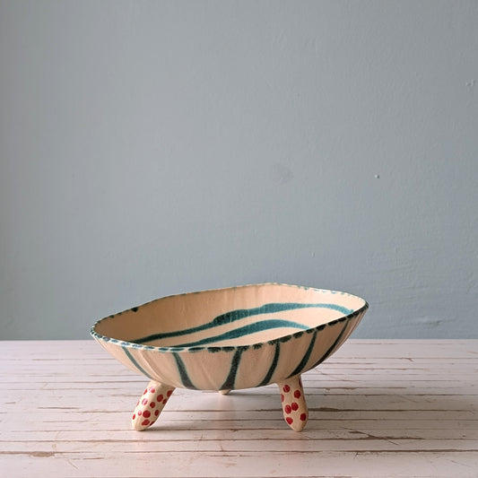 Front view of a white footed ceramic bowl with green stripes on a white wooden table.