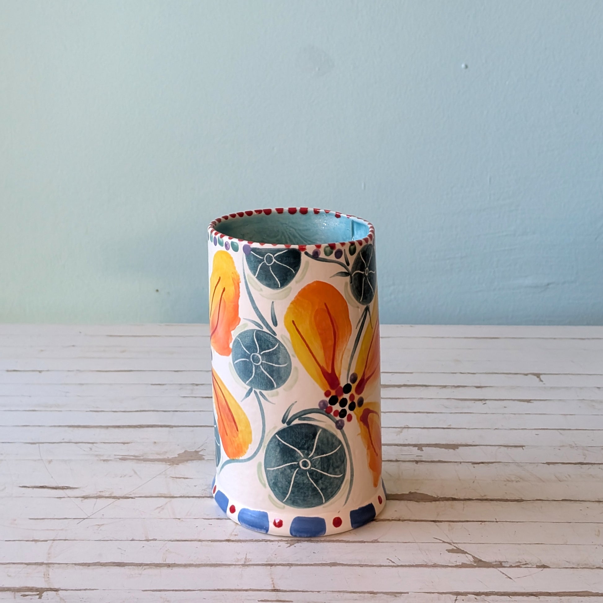 Side and top view of a white ceramic vase with orange, green and blue floral pattern and blue interior