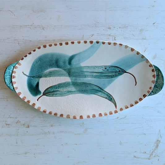 Oval ceramic platter with green leaf design on a white surface