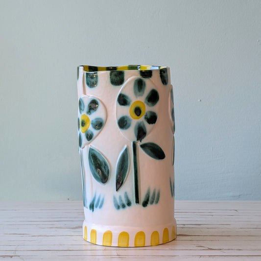 Front view of a white ceramic vase with a green and yellow raised floral motif