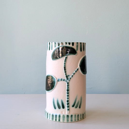 Cylindrical ceramic vase with abstract green patterns on a light blue background
