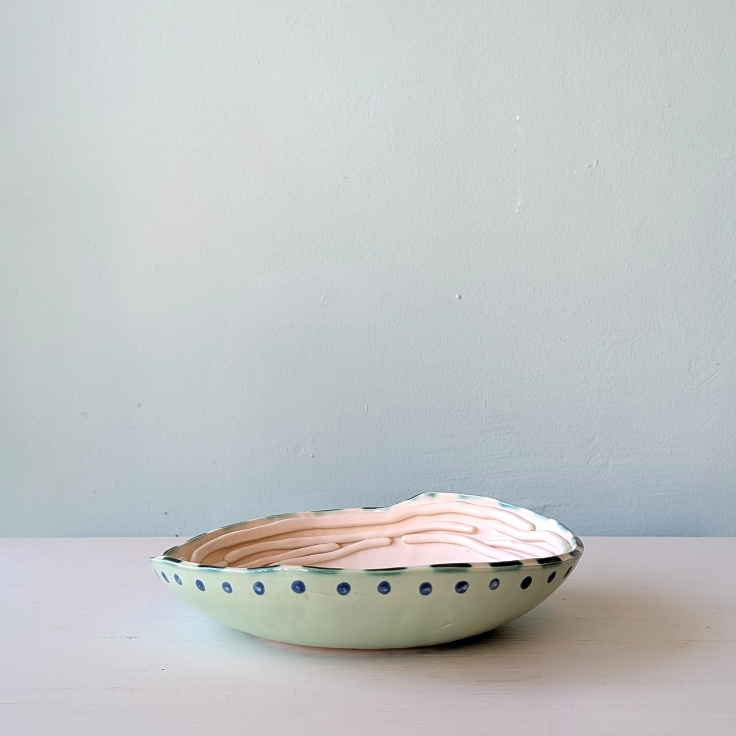 Ceramic bowl with wavy design and blue dots on a light gray background