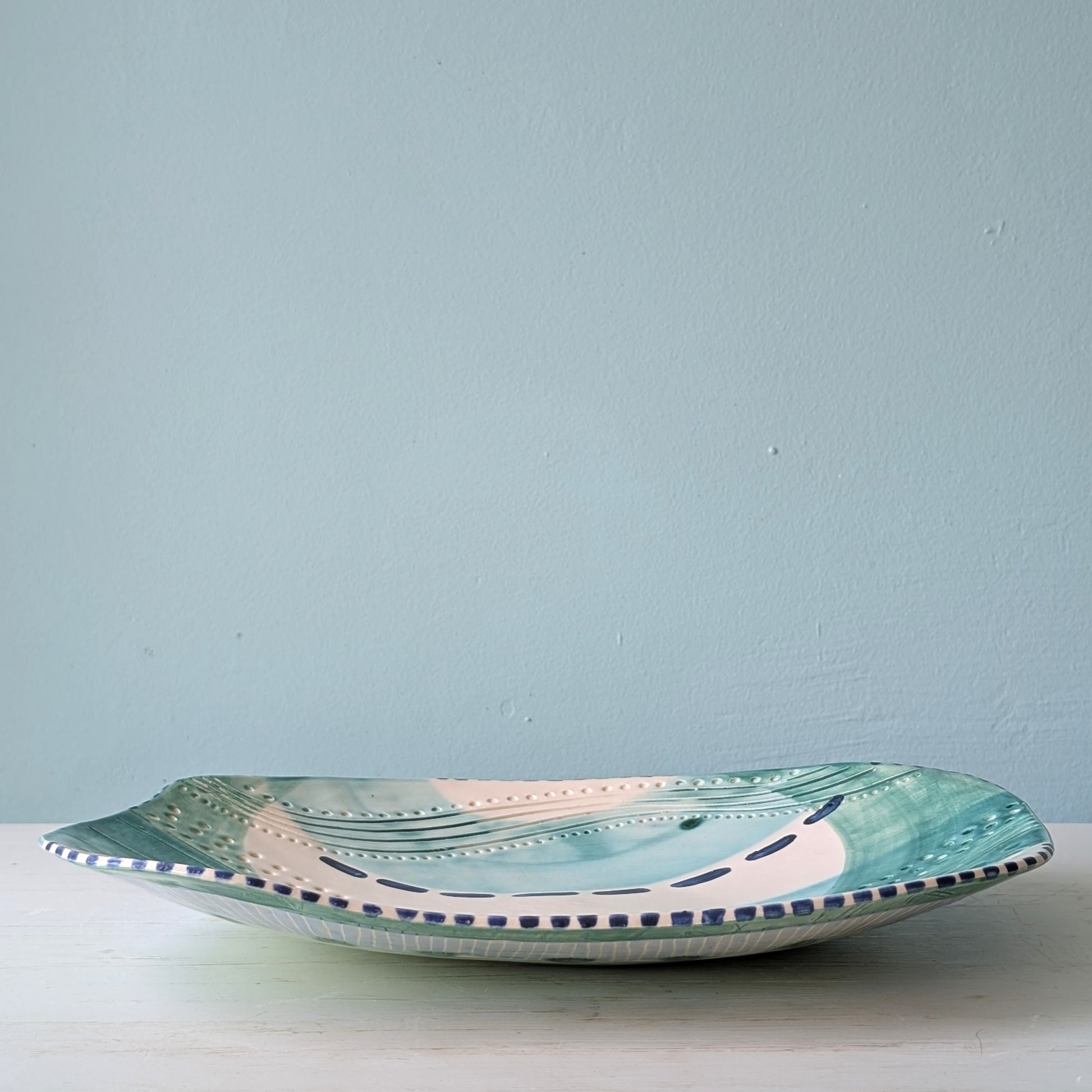 Ceramic plate with decorative edge on a light surface against a light blue wall