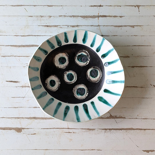 Top view of a white ceramic bowl with green abstract pattern on a white wooden surface.