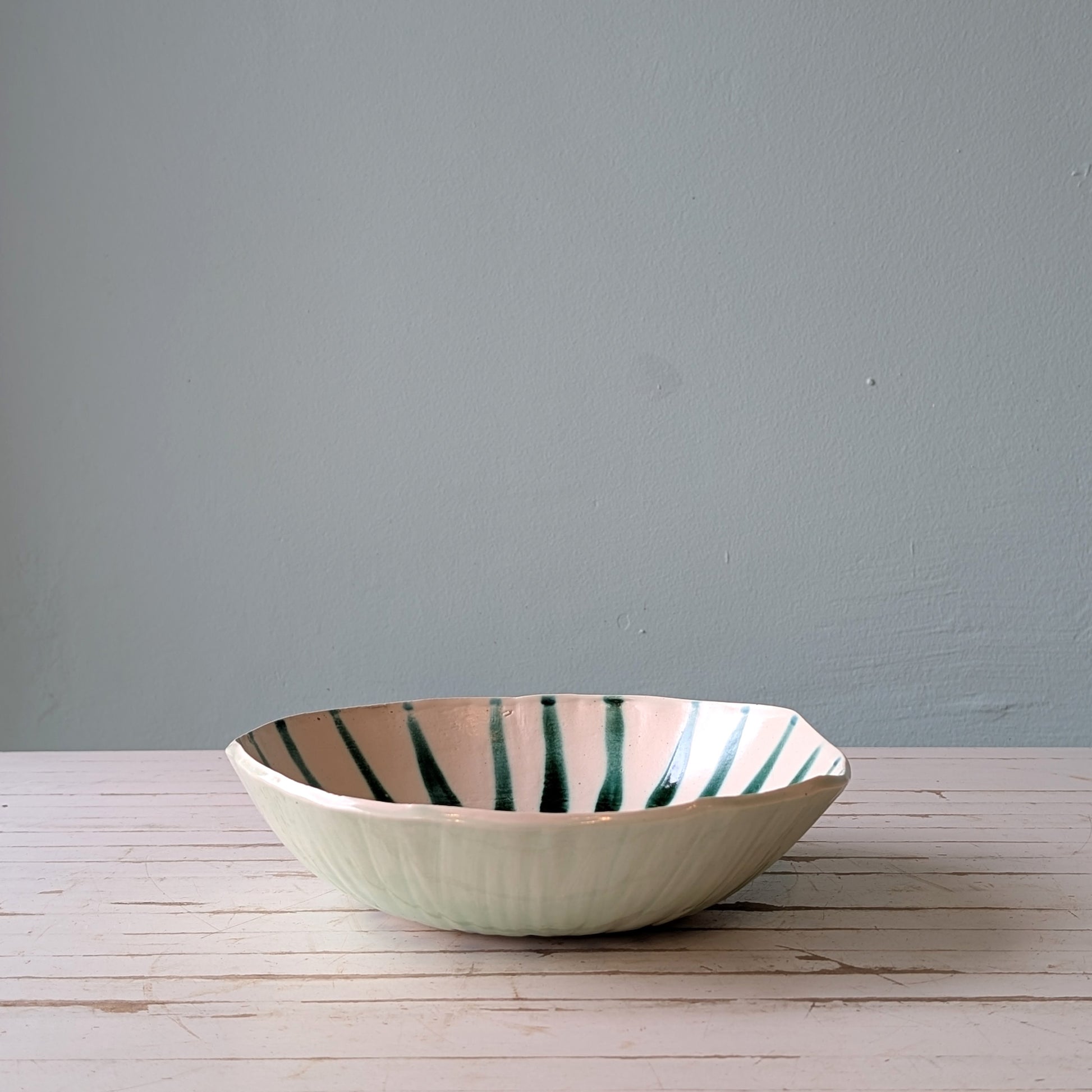Front view of a white ceramic bowl with green abstract pattern on a white wooden table with blue background.