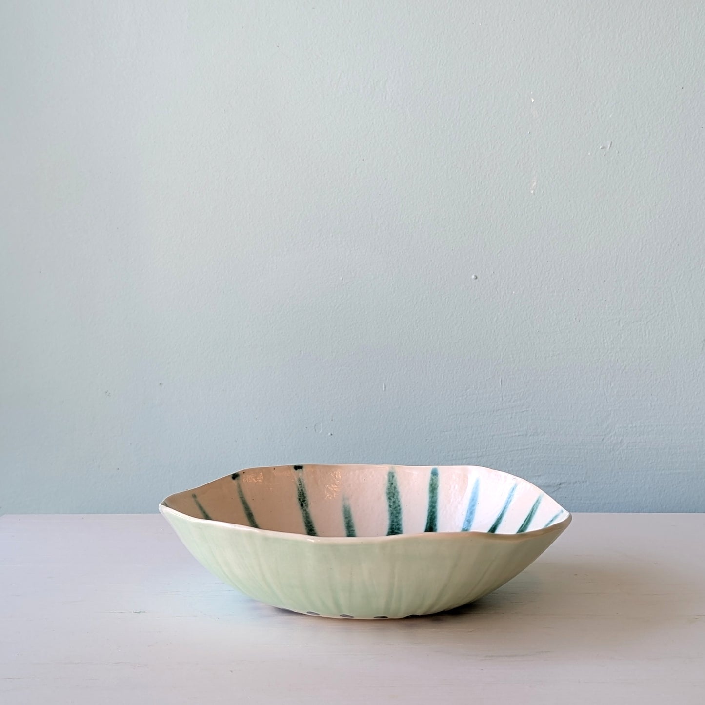 Ceramic bowl with green stripes on a white surface and blue background