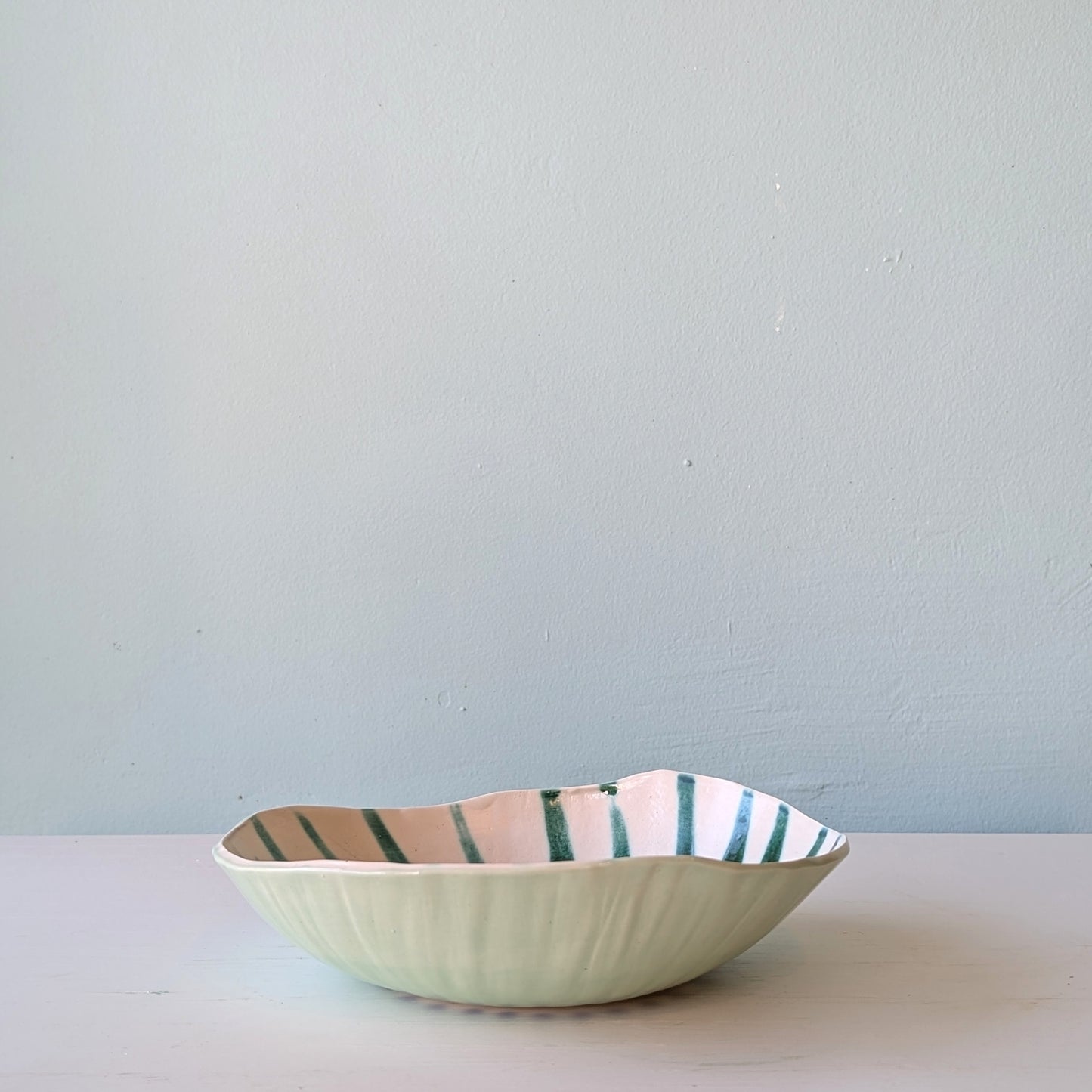 Ceramic bowl with striped pattern on a light surface and light blue background