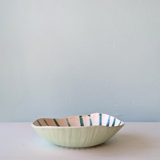 Ceramic bowl with striped pattern on a light surface and light blue background