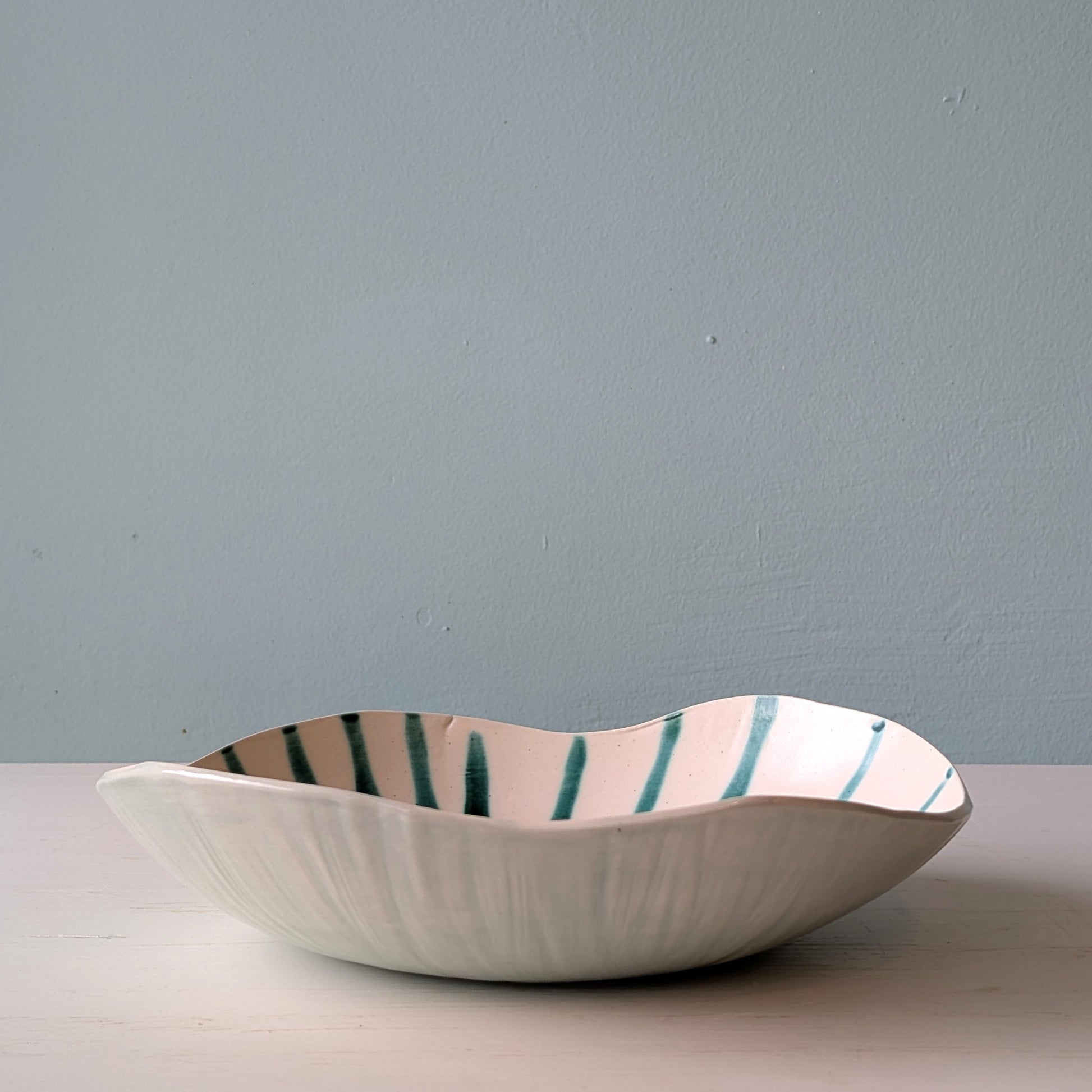 Striped green and white ceramic bowl on a white table against a blue wall
